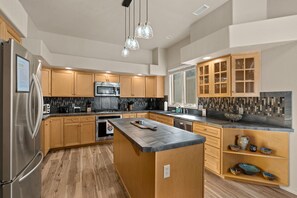 A modern kitchen with wooden cabinets, a central island, stainless steel appliances, and a backsplash with mosaic tiles. - Golf Course, Hot Spring Close, Dalton Ranch! (Durango)