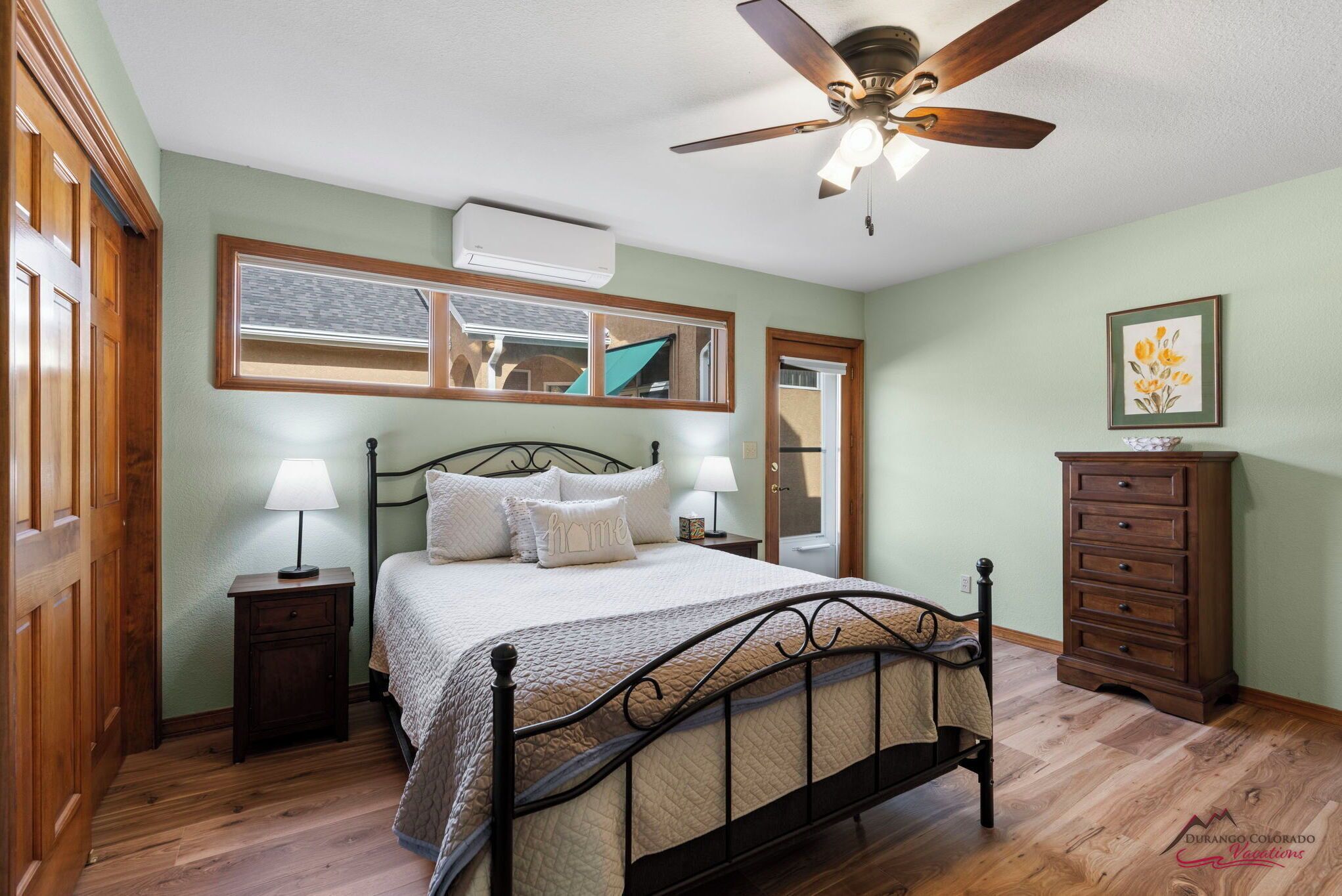 Une chambre à coucher avec un lit, deux tables de chevet avec des lampes, une commode, un ventilateur de plafond et un grand miroir au-dessus du lit.
