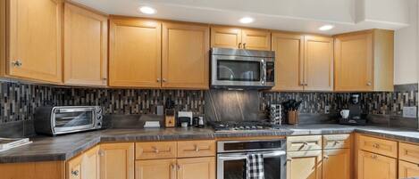 A modern kitchen with wooden cabinets, a stainless steel range, a microwave, a toaster, and a tiled backsplash.