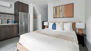 A modern hotel room with a large bed, a kitchen area with a refrigerator, and a wall-mounted abstract painting. - The Jardín | Spanish Studio | Foodie Row (Portland)