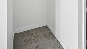 A corner of a room with white walls, a concrete floor, and a wooden hanger rod. - The Jardín | Spanish Studio | Foodie Row (Portland)