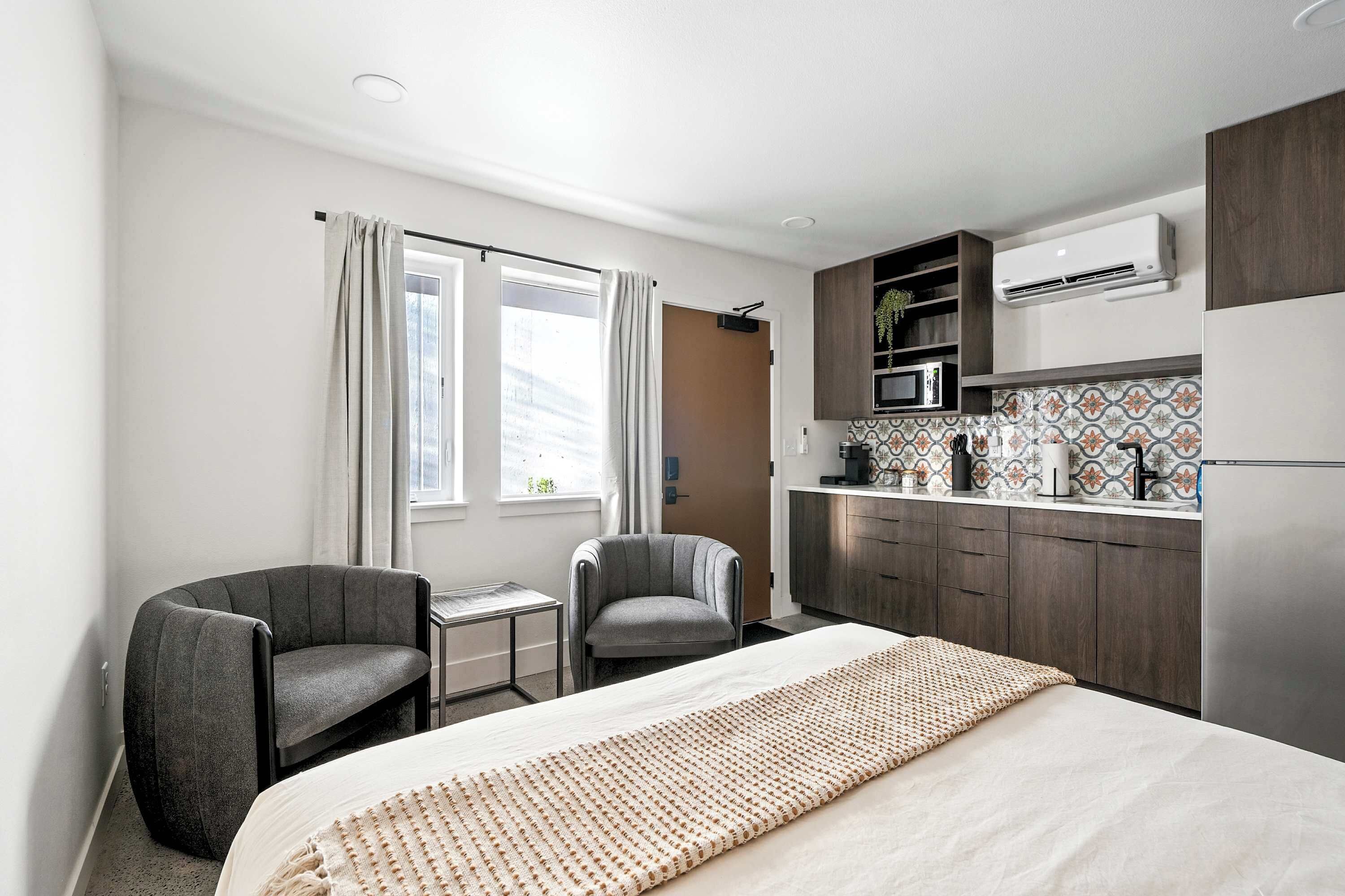 Une chambre d’hôtel moderne équipée d’un lit, de deux fauteuils, d’une petite table et d’une kitchenette.
