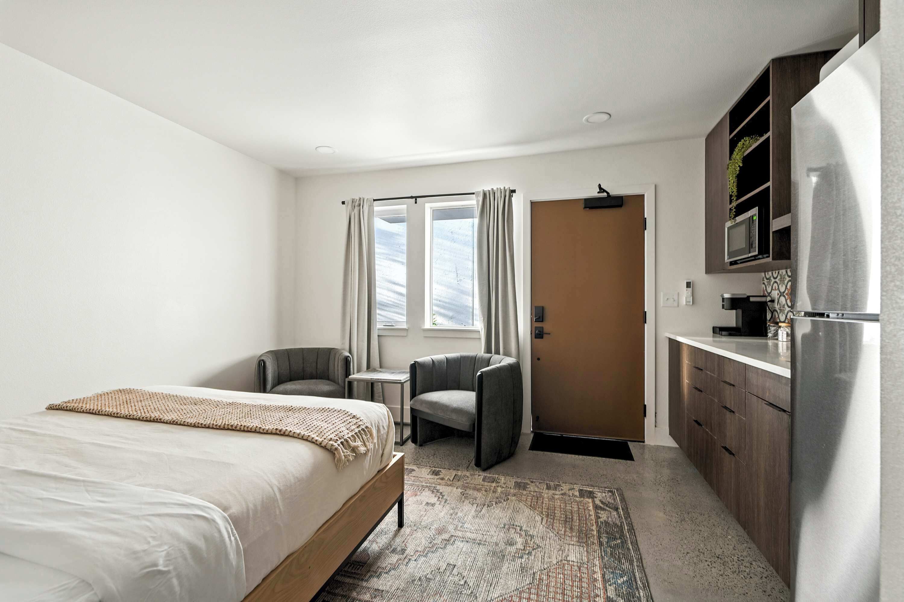 Een hotelkamer met een bed, een bureau, een stoel, een kitchenette en een deur.