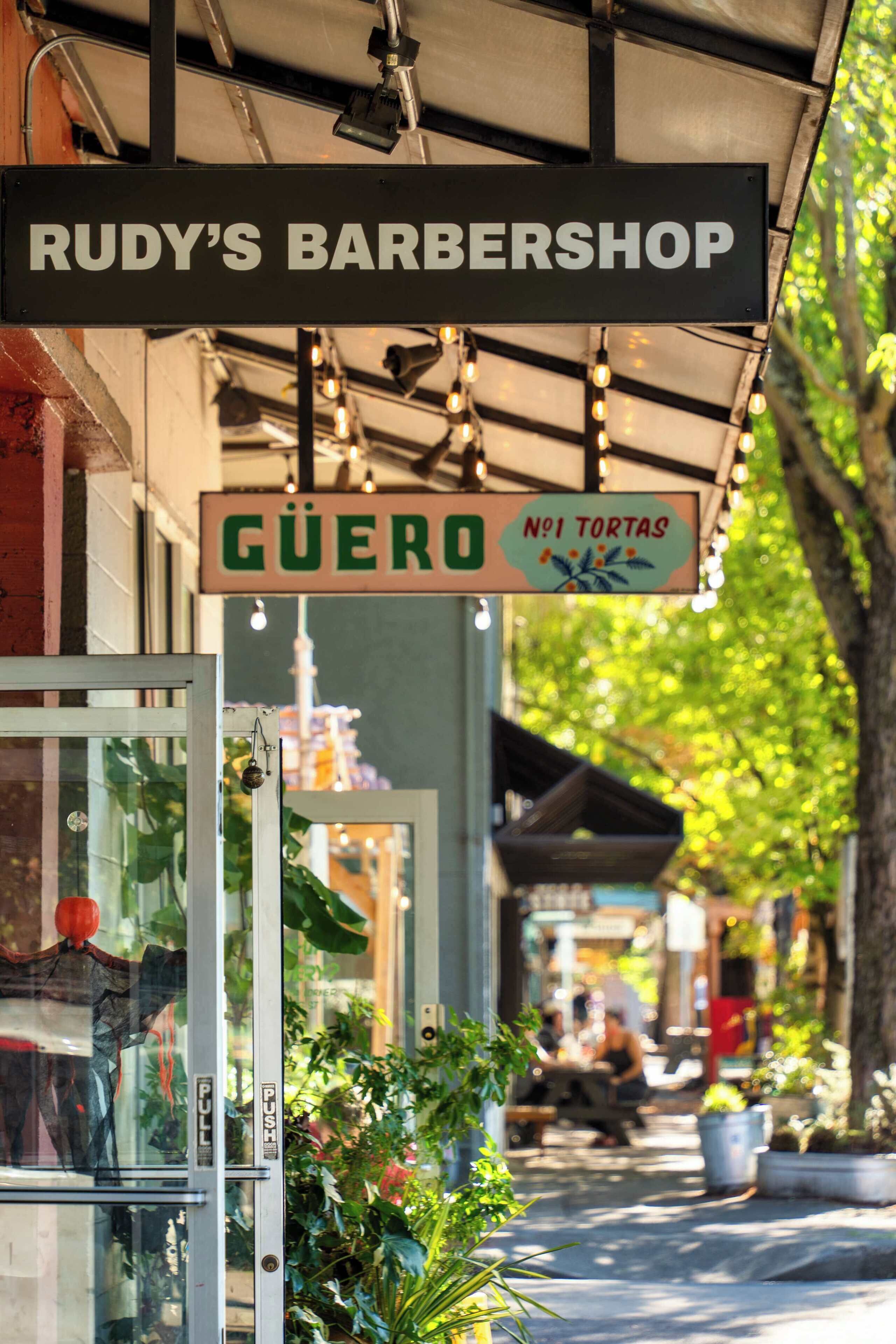 Off-property: Rudy's Barbershop and Güero signs along the sidewalk.
