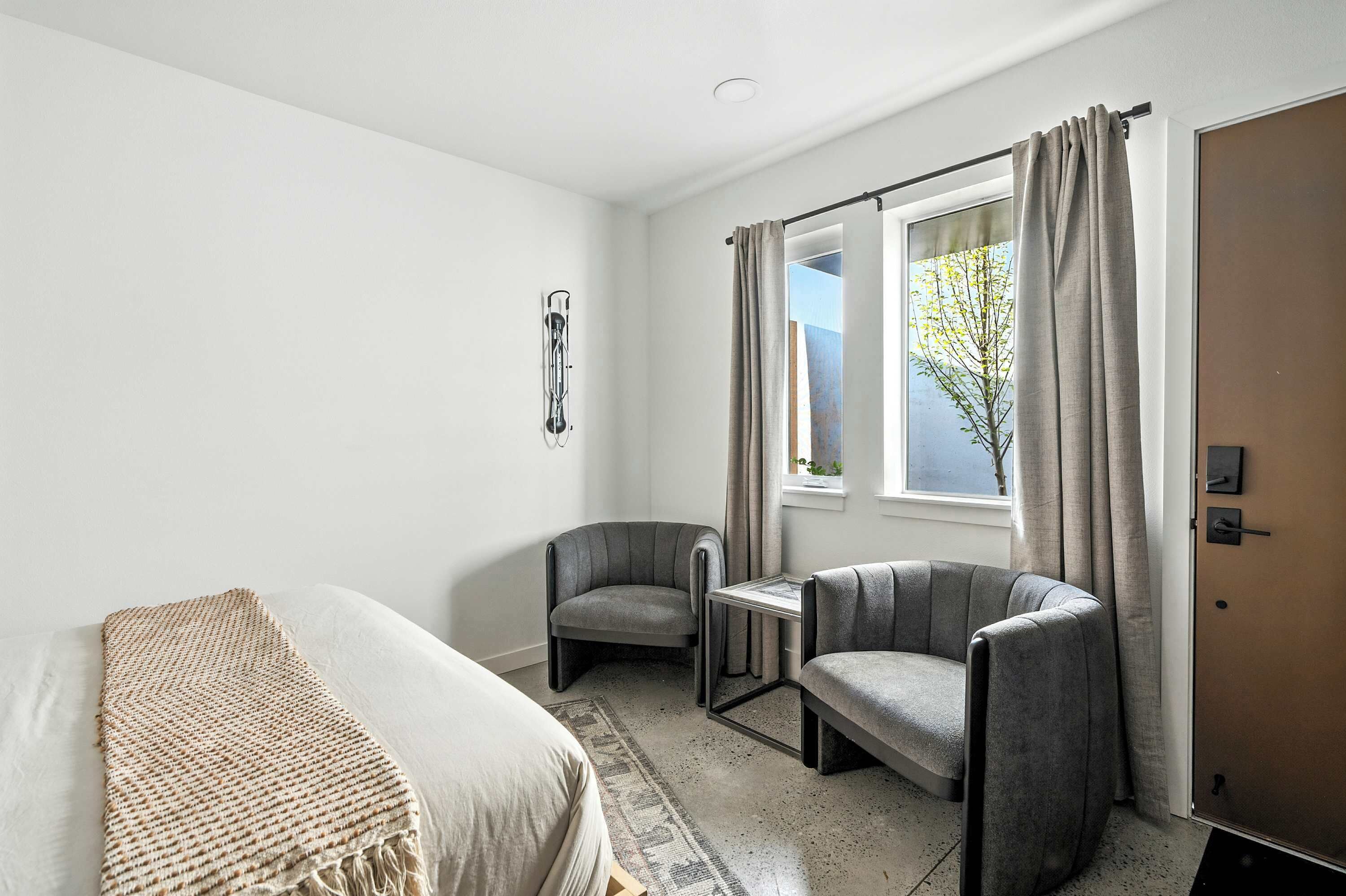 Une chambre d’hôtel moderne, équipée d’un lit, de deux fauteuils, d’une petite table et d’une fenêtre avec des rideaux.
