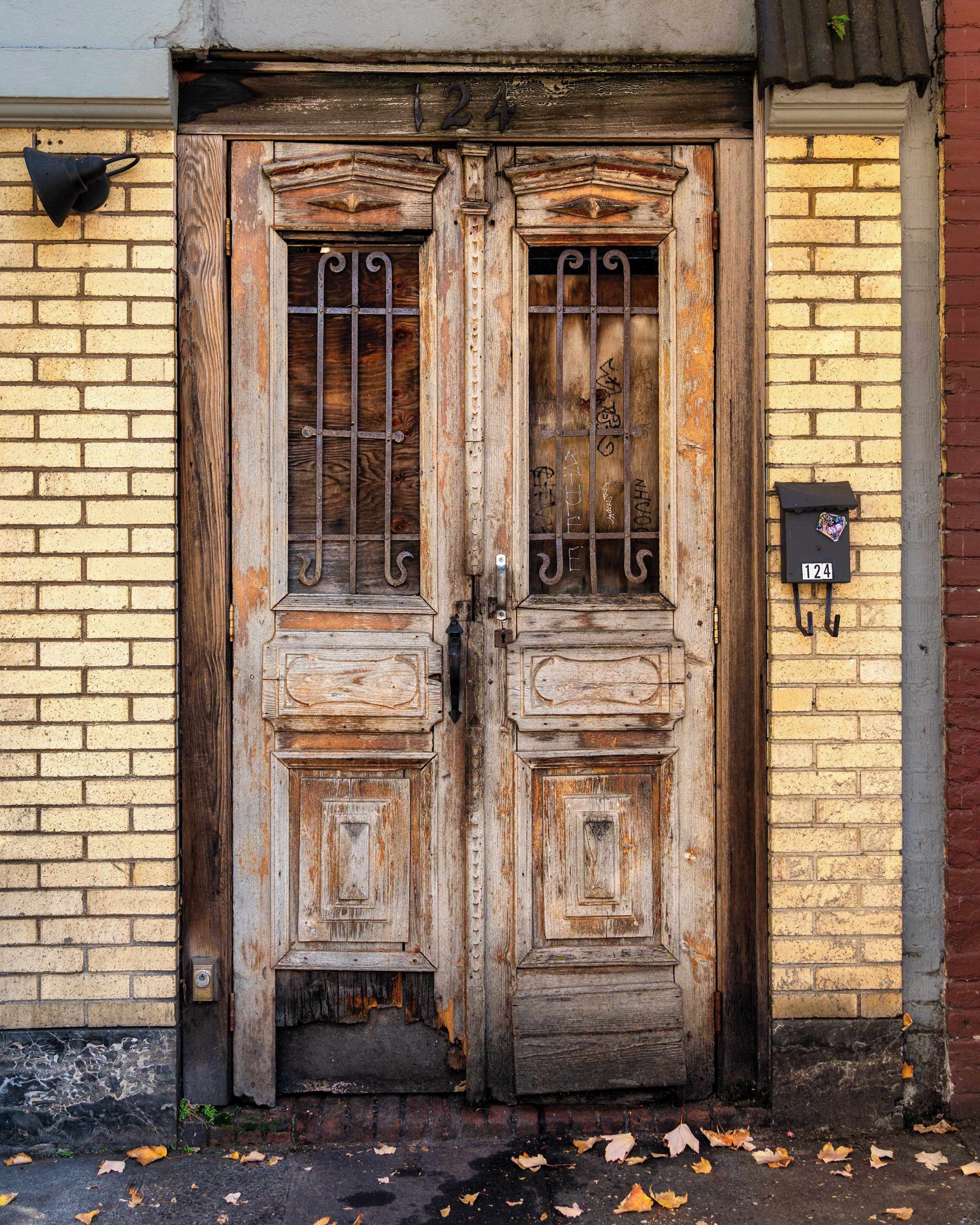 Une porte à deux battants en bois, usée par les intempéries, surmontée d’un portail en métal, le tout intégré dans un bâtiment en briques.