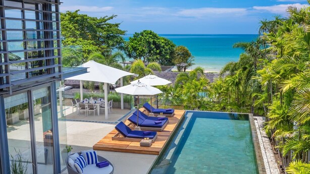 A modern outdoor pool area with lounge chairs and umbrellas, overlooking a clear blue ocean.