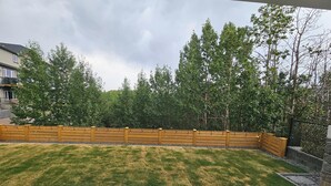 A backyard with a wooden fence, a grassy lawn, and a stone pathway. - New Modern Suite in Calgary NW (Calgary)