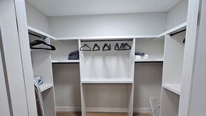A walk-in closet with white shelves and hangers, a wooden floor, and a white chair. - New Modern Suite in Calgary NW (Calgary)