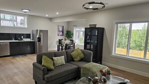 A modern living room with a grey sofa, a glass coffee table, and a dining area with a table and chairs. - New Modern Suite in Calgary NW (Calgary)