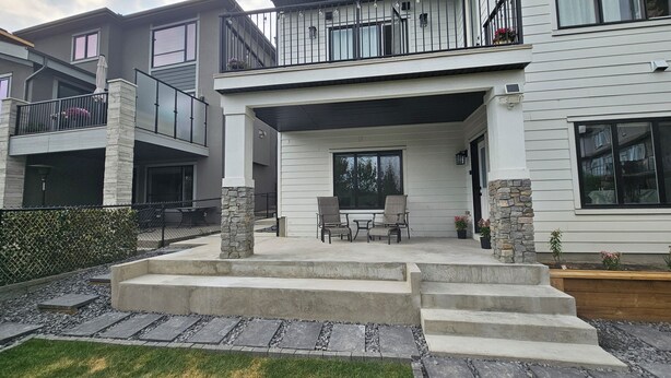 A modern two-story house with a covered patio, stone pillars, and a small outdoor seating area. - New Modern Suite in Calgary NW (Calgary)