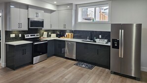 A modern kitchen with grey cabinets, stainless steel appliances, and a window providing natural light. - New Modern Suite in Calgary NW (Calgary)