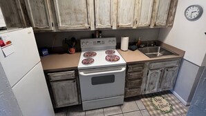 Une cuisine de taille réduite, avec des meubles blancs, une cuisinière, un évier et une horloge au mur.