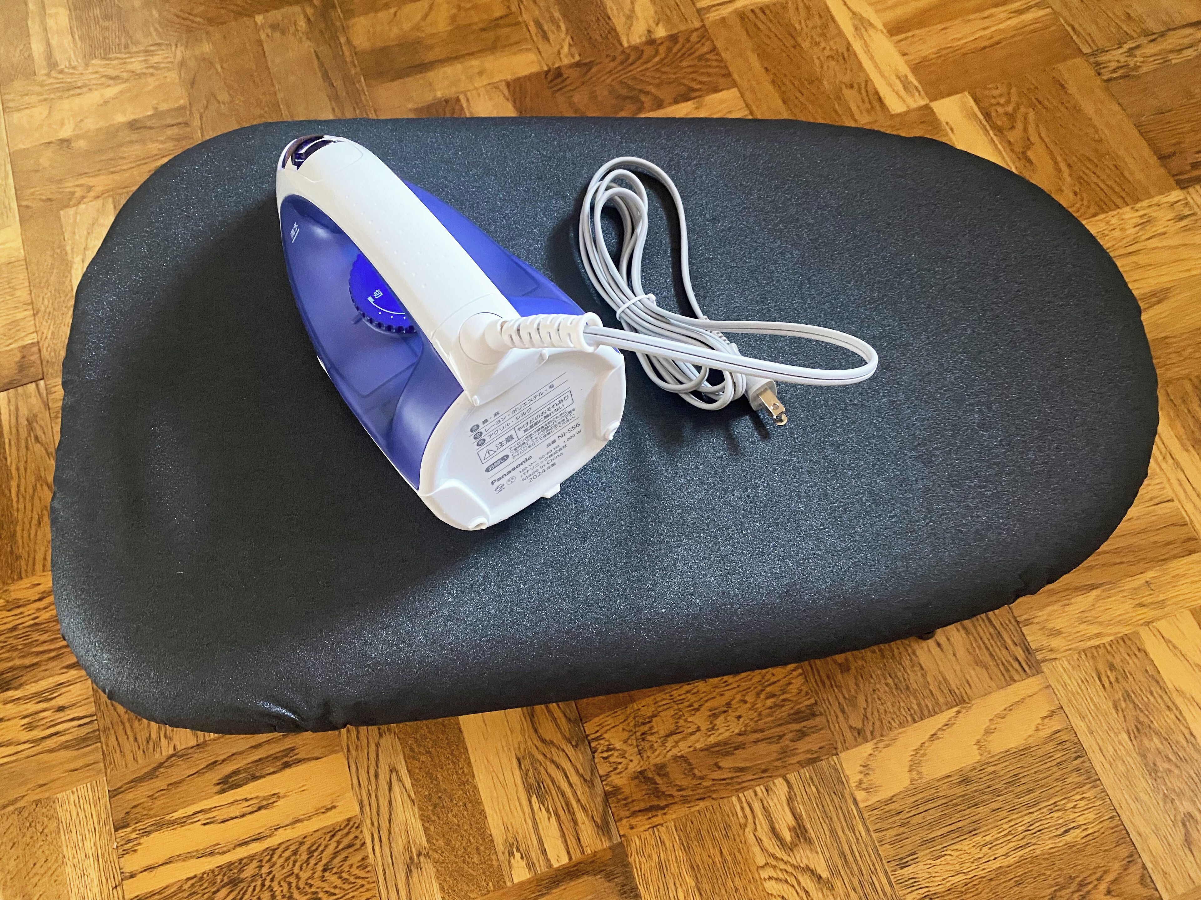 Ein tragbares Bügeleisen mit Kabel und Netzteil auf einer schwarzen Matte.