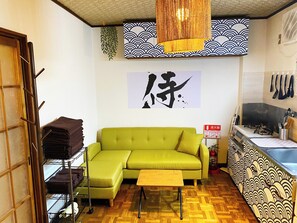 A compact living space with a green sofa, a wooden coffee table, and a kitchen area with a gas stove. - Nostalgic Japan! Direct to Shinjuku & Shibuya on JR Station. (Kita City, Ukima)