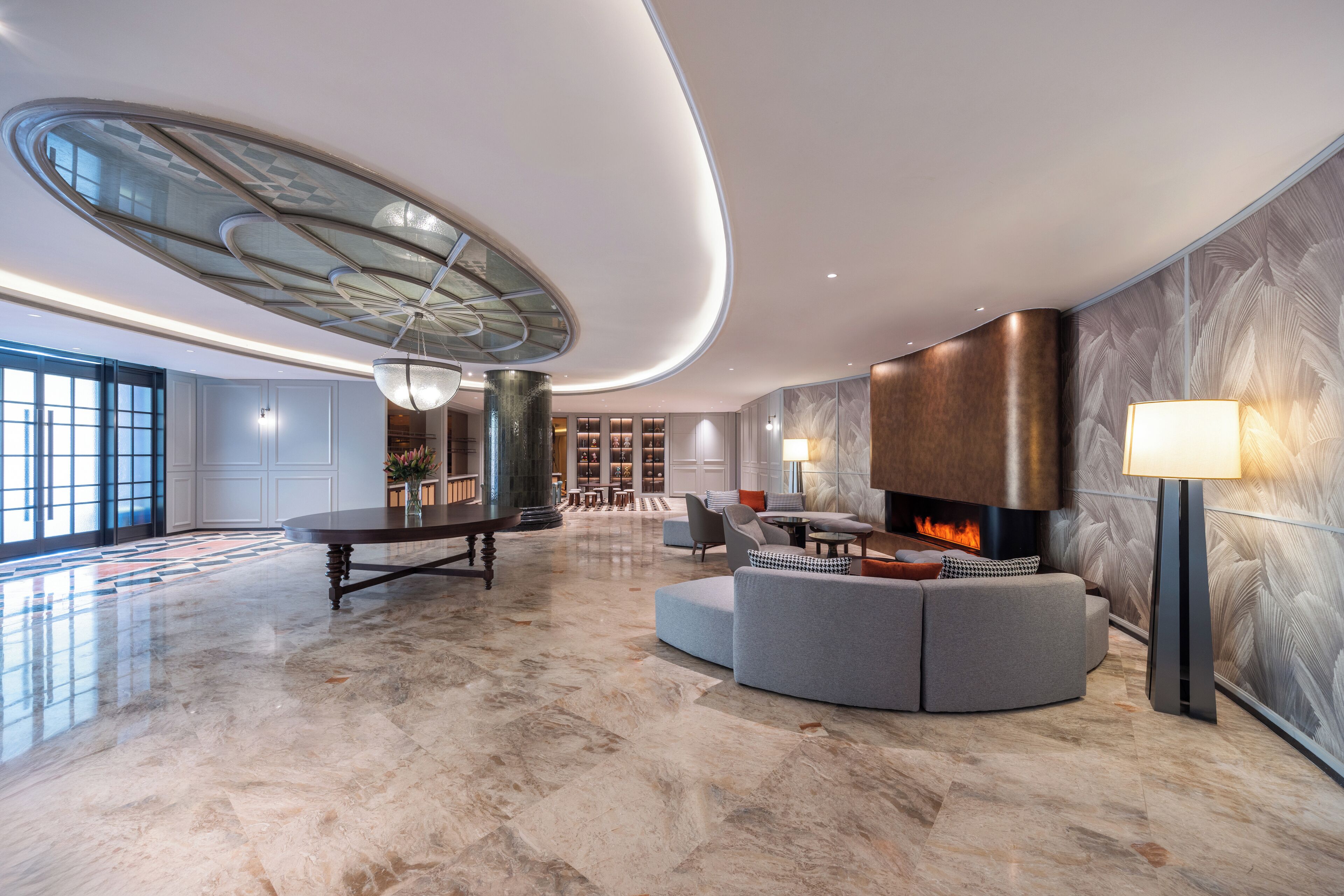 A spacious lobby with a marble floor, a central seating area with a fireplace, and a modern ceiling design.