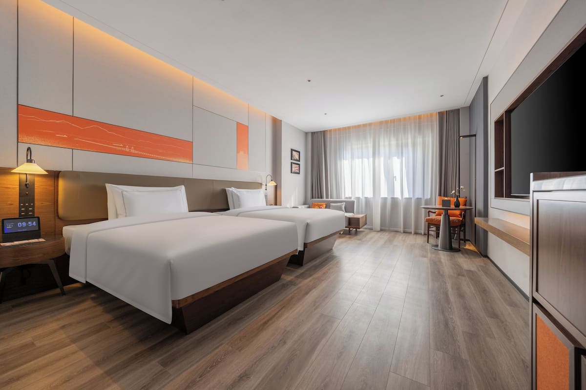 Une chambre d’hôtel moderne équipée de deux lits, d’un bureau, d’une chaise, d’une télévision et d’une grande fenêtre avec des rideaux.