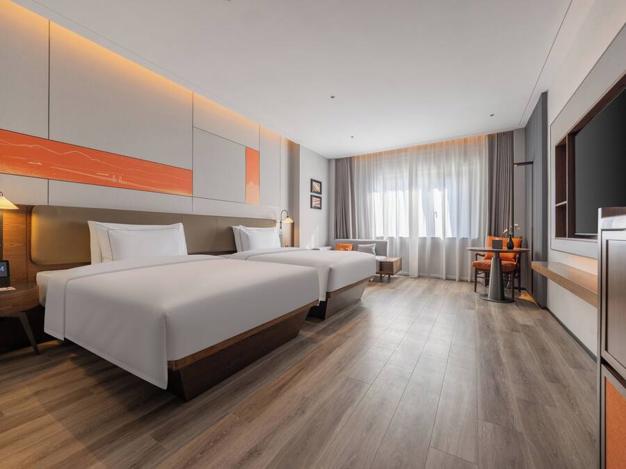 Een moderne hotelkamer met twee bedden, een bureau, een stoel, een televisie en een groot raam met gordijnen.