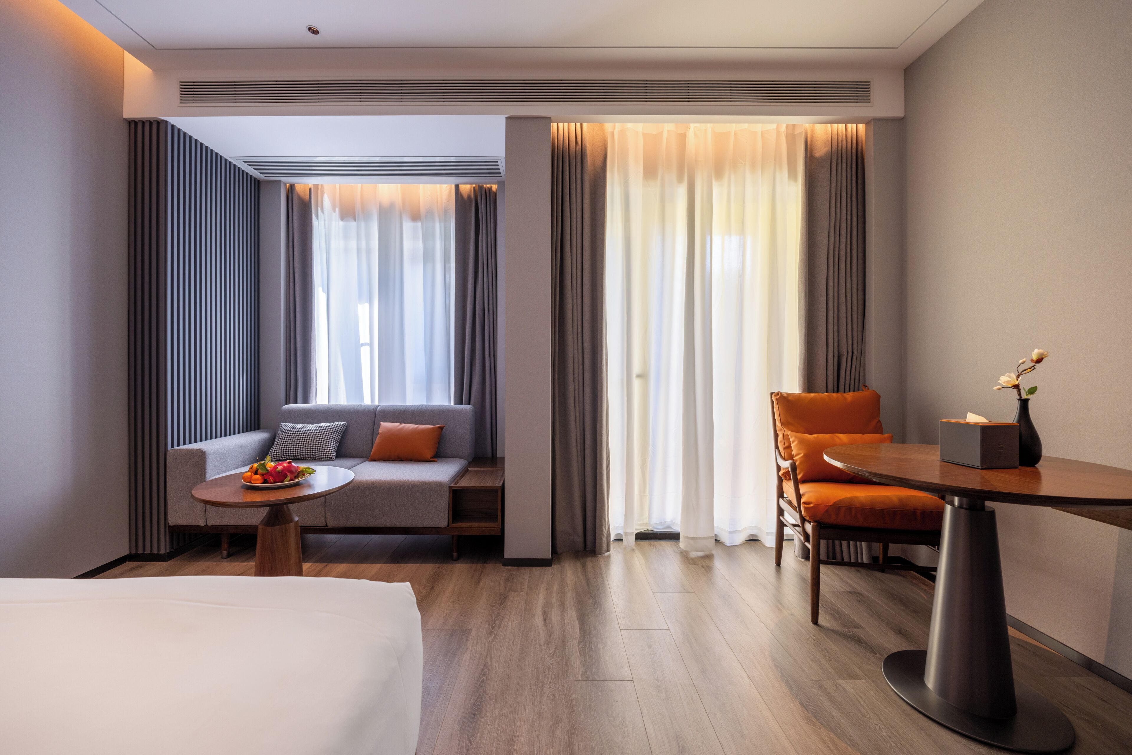 A modern hotel room with a bed, a sofa, a dining table, and a chair.
