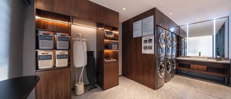 A modern hotel bathroom with wooden cabinetry, a washing machine, and a sink.