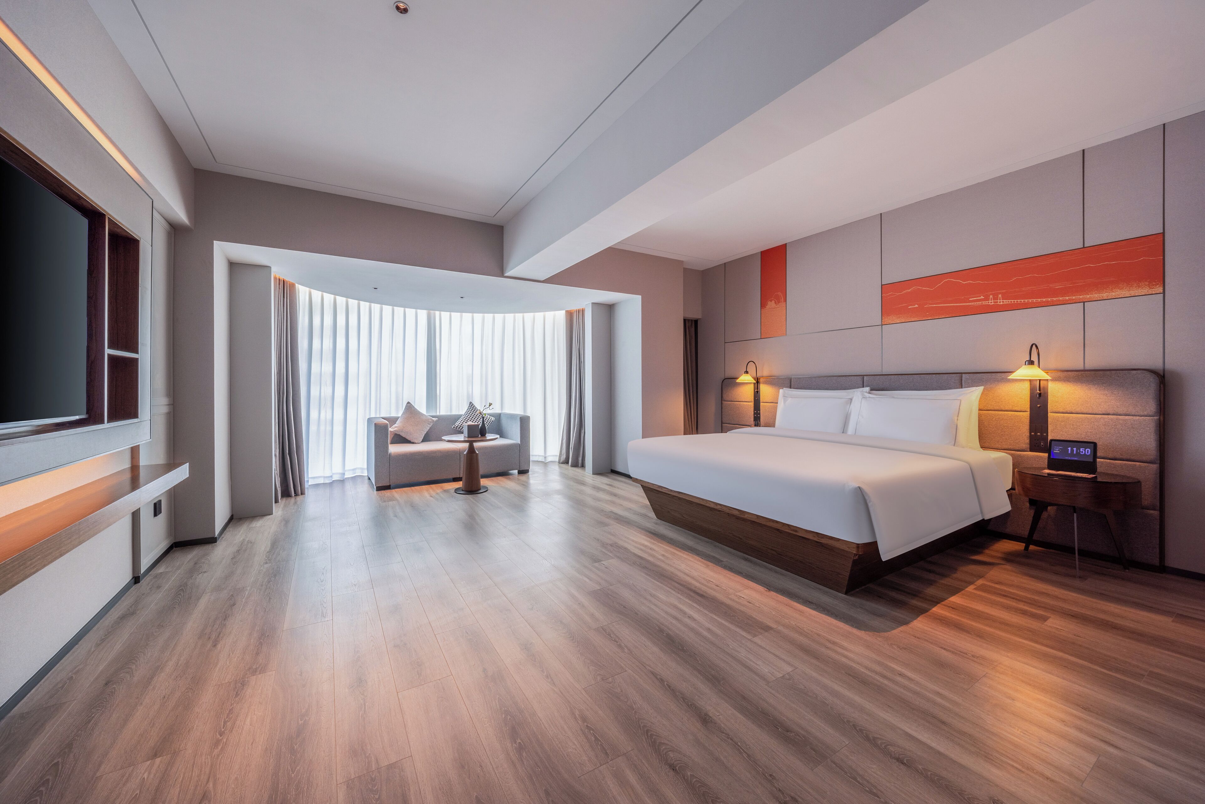 A modern hotel room with a large bed, a TV, a sofa, and a desk.