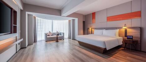 A modern hotel room with a large bed, a TV, a sofa, and a desk.