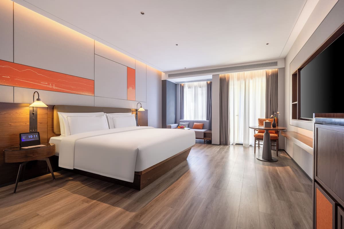 Une chambre d’hôtel moderne, dotée d’un grand lit, de tables de chevet, d’un bureau et d’une télévision.
