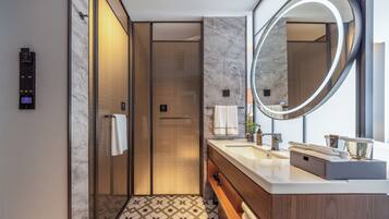 A modern bathroom with a large mirror, two sinks, a towel rack, and a shower area.