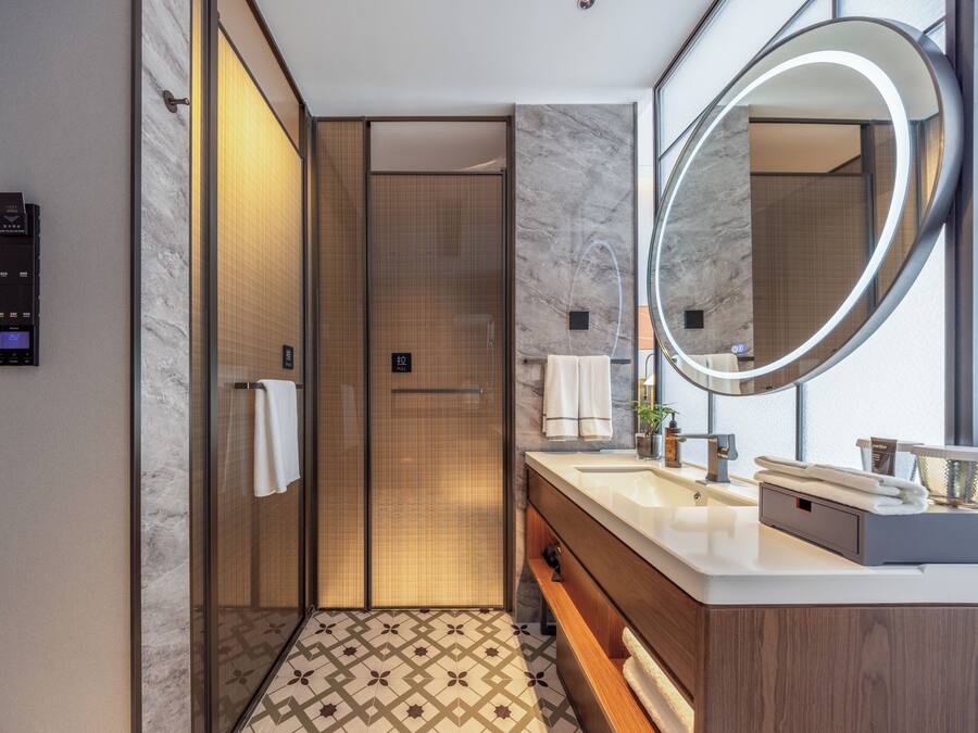 A modern bathroom with a large mirror, two sinks, a towel rack, and a shower area.