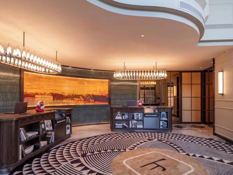 Een moderne lobby met een groot, rond tapijt met een patroon, een receptiebalie en een wandgemonteerd scherm.