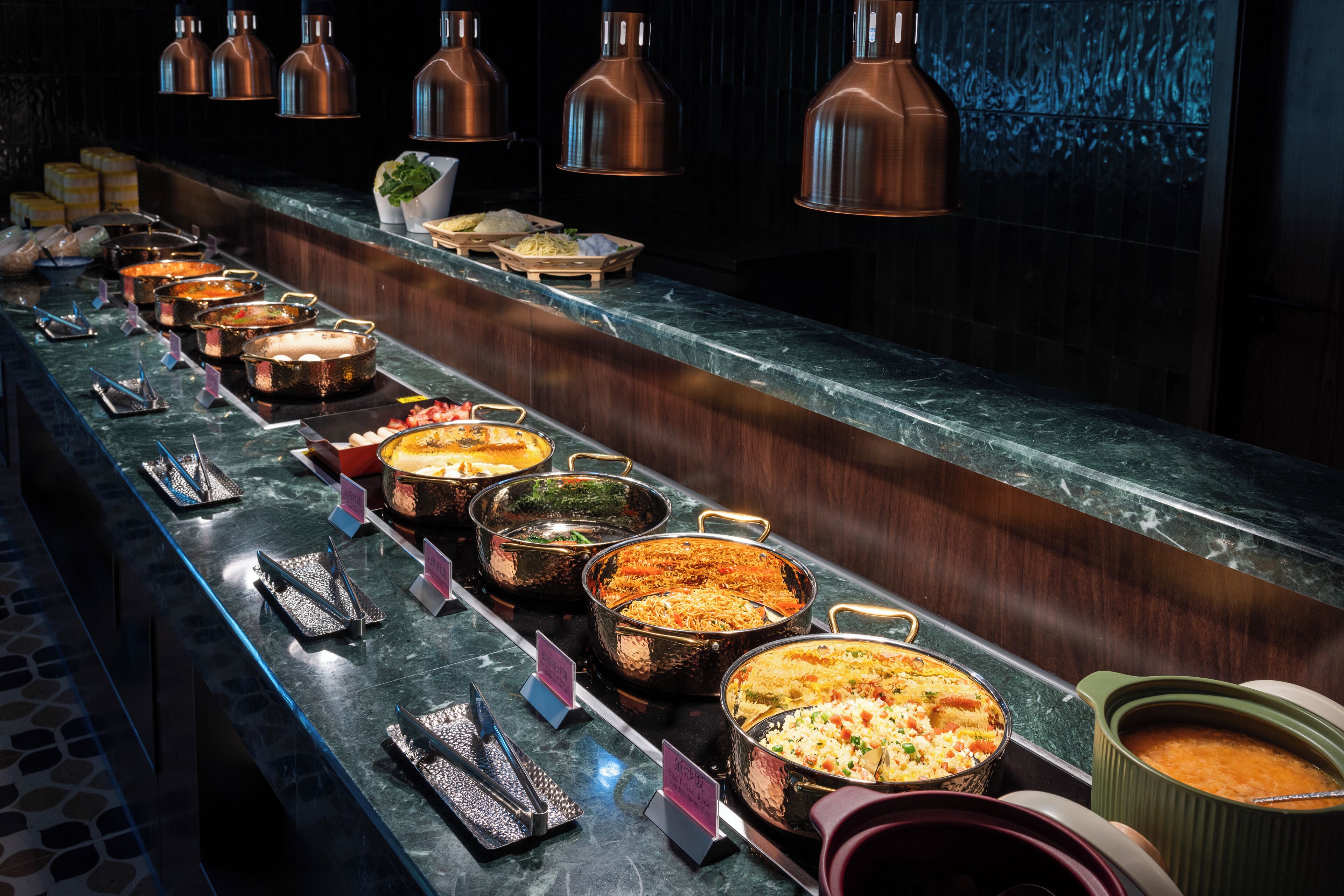 A buffet line with various dishes and a marble countertop.