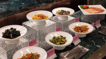 A buffet with various dishes displayed on marble counters, each labeled with a pink sign.
