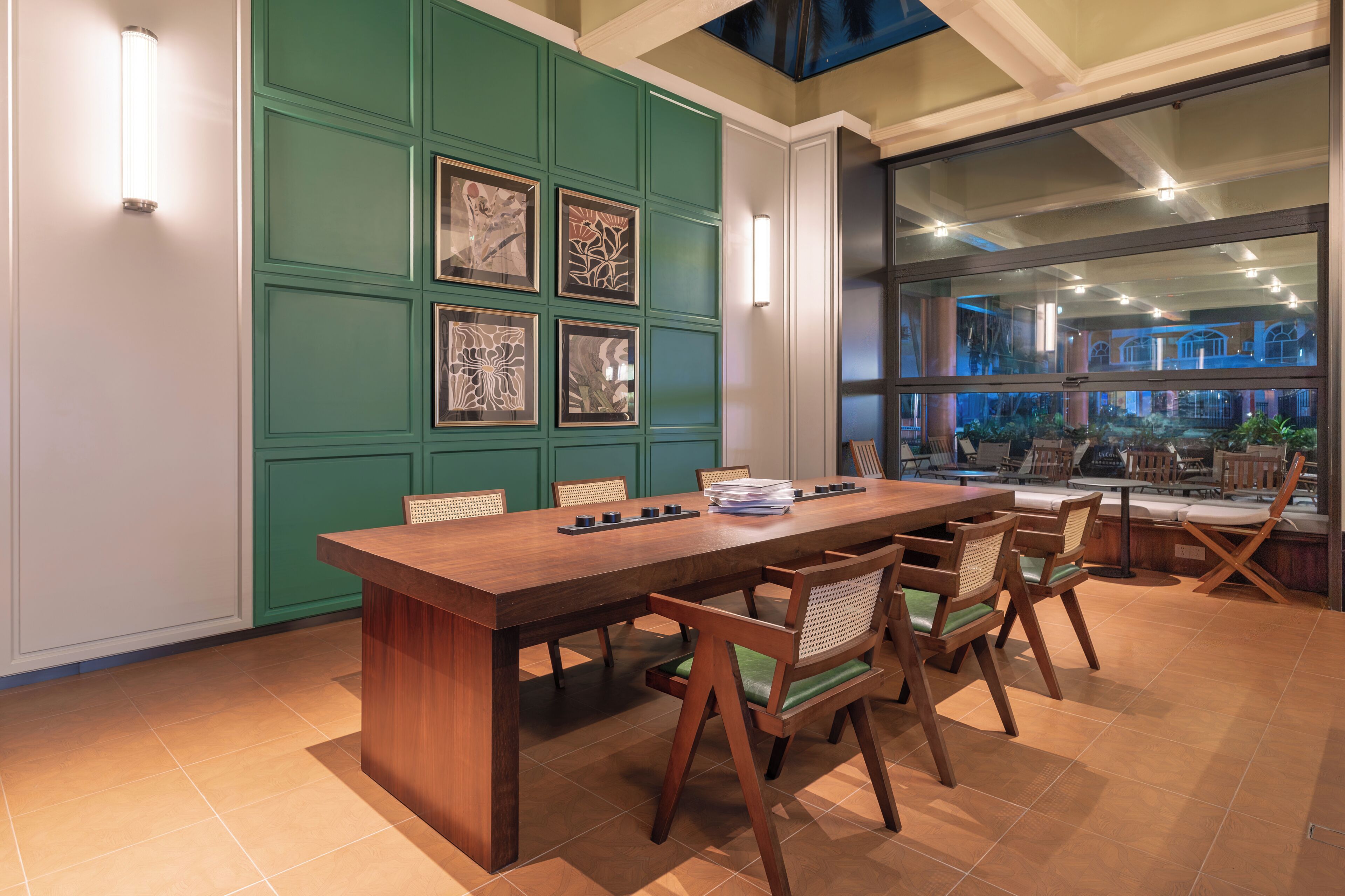 A conference room with a long wooden table, six chairs, and framed artwork on the green wall.