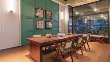 A conference room with a long wooden table, six chairs, and framed artwork on the green wall.