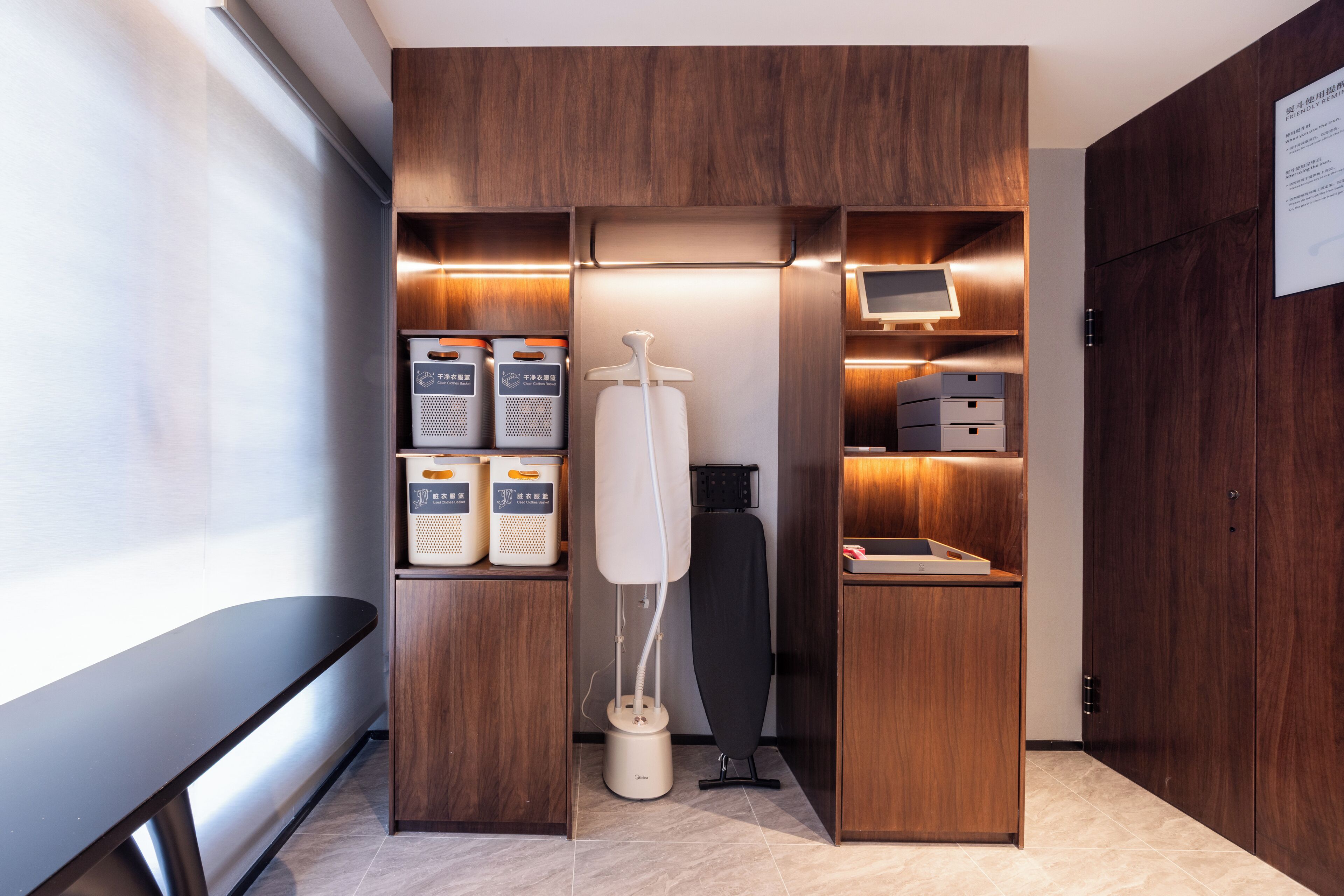 Une chambre compacte et moderne, dotée de meubles en bois, d’un espace intégré pour repasser et d’un petit bureau.