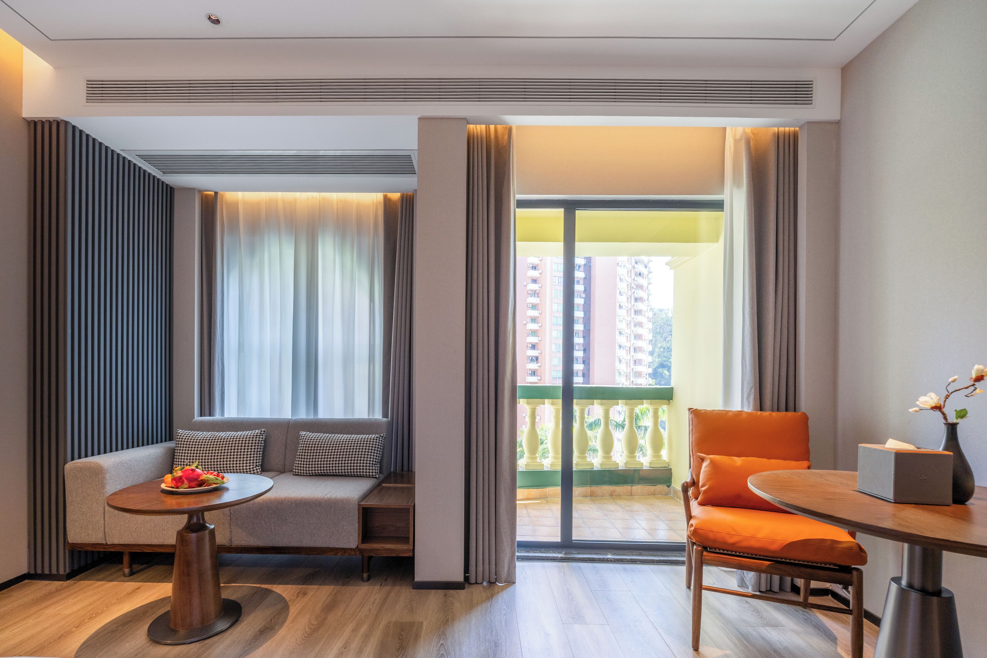 Une chambre d’hôtel moderne, dotée d’un canapé, d’une petite table ronde, d’une chaise et d’un balcon offrant une vue sur les gratte-ciel.