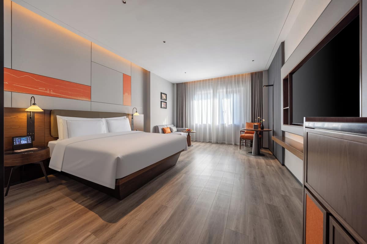 Une chambre d’hôtel moderne dotée d’un grand lit, de tables de chevet, d’une télévision et d’un coin salon avec une table et des chaises.