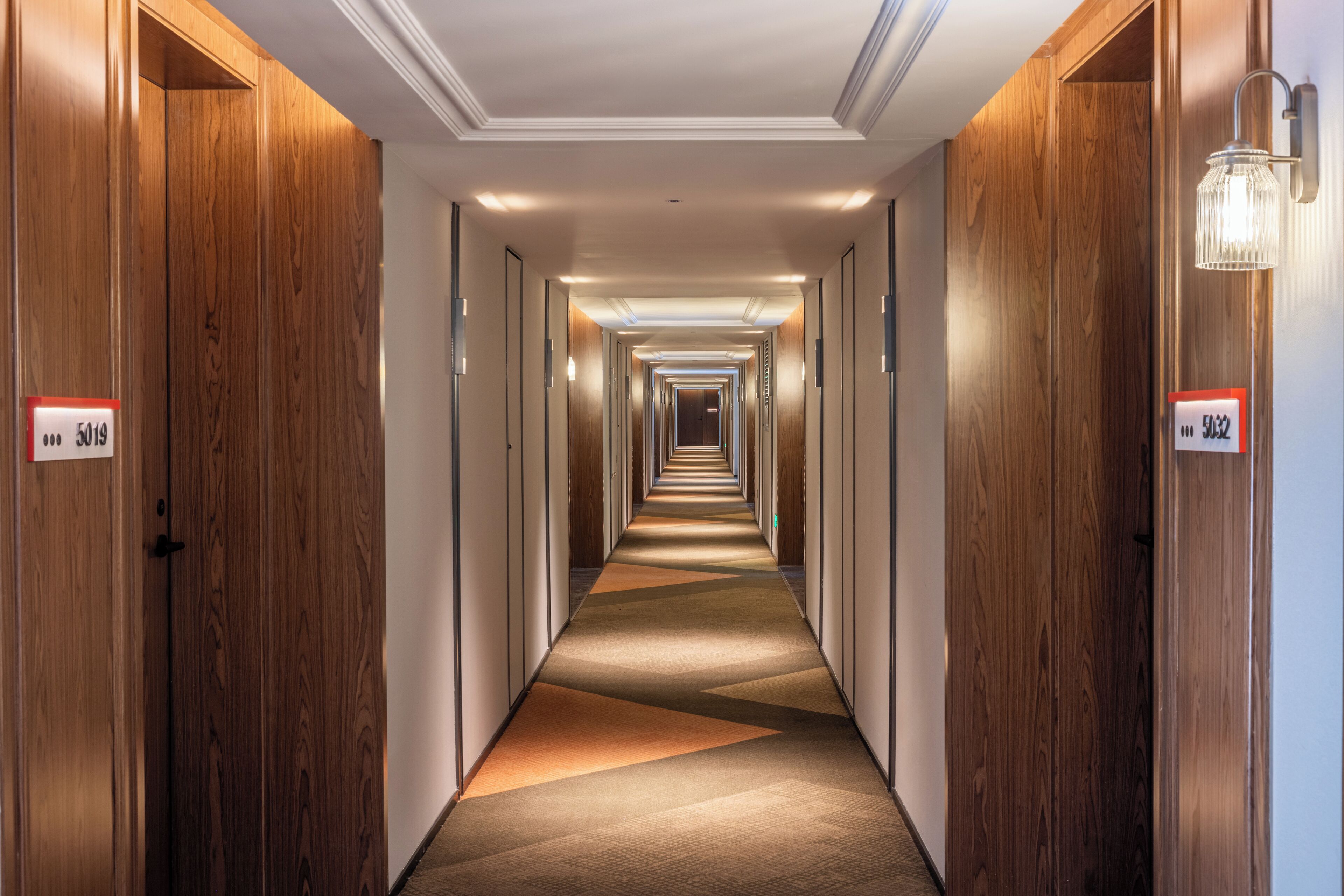 A hotel hallway with wooden doors, numbered room signs, and a carpeted floor.