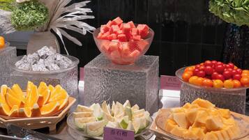 A fruit display with various types of fruits in bowls and plates, including watermelon, oranges, and tomatoes.