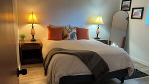 Una camera da letto ordinata con un letto, due comodini, lampade, uno specchio e una piccola pianta.