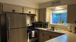 Una cucina con elettrodomestici in acciaio inossidabile, una finestra con piante in vaso e un cartello che indica che si tratta di una cucina.