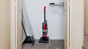 Un placard dont les portes sont ouvertes, un aspirateur et un portant à vêtements.
