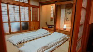 A traditional Japanese room with tatami flooring, two beds with white bedding, a shoji screen door, and a small table with a lamp. - In a quiet, green environment, with free parking, your room is in the middle of the ocean, you have your own spacious wooden room, a spacious living room with outdoor seating, and your own private garden with a roast fireplace. (由布市湯布院町川上)