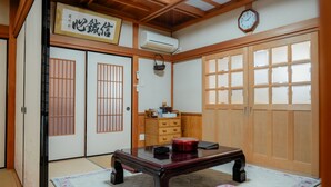 A traditional Japanese room with tatami flooring, a wooden table, a red cushion, sliding doors, and a clock on the wall. - In a quiet, green environment, with free parking, your room is in the middle of the ocean, you have your own spacious wooden room, a spacious living room with outdoor seating, and your own private garden with a roast fireplace. (由布市湯布院町川上)