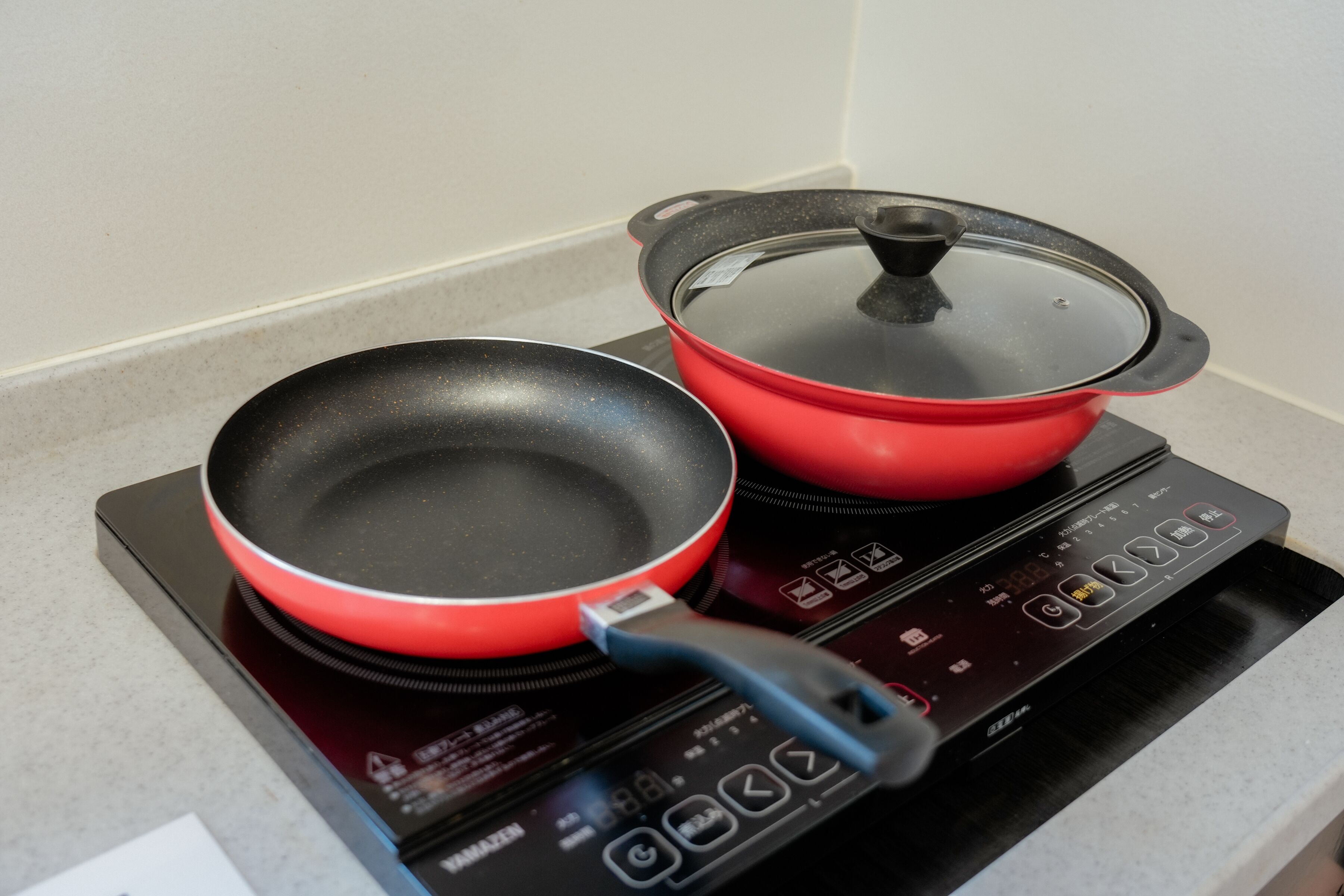 A kitchen with a red induction cooktop and a black frying pan on it.