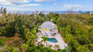 Une maison à deux étages avec une piscine, entourée d’une végétation tropicale luxuriante et offrant une vue sur l’océan.