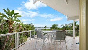 Une terrasse extérieure couverte, avec une table ronde et quatre chaises, entourée d’une balustrade blanche, et offrant une vue sur une étendue d’eau et une végétation luxuriante.