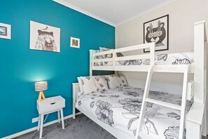 A bunk bed with floral bedding, a bedside table with a lamp, and a wall with framed pictures. - Apollo's Rest. (Apollo Bay)