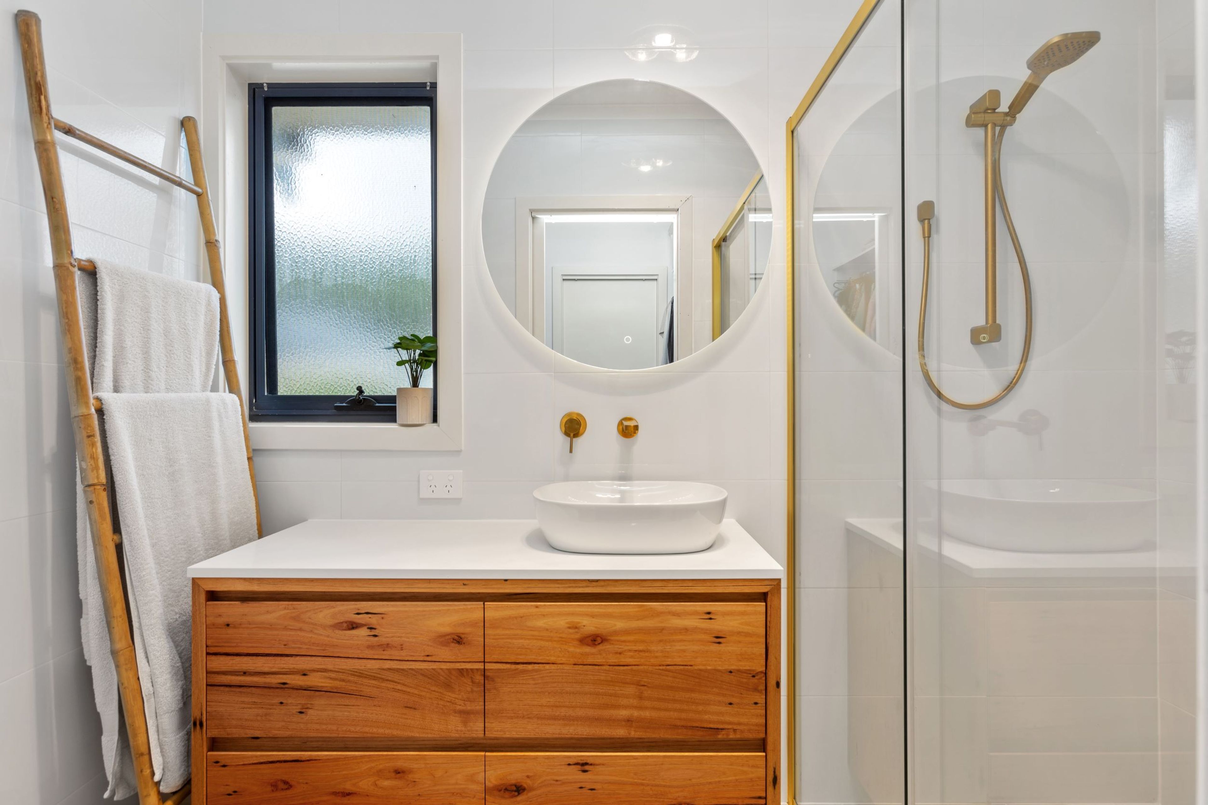 A bathroom with a wooden vanity, a round mirror, a white sink, and a glass-enclosed shower.