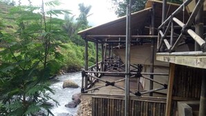 Un puente de bambú sobre un río, con una estructura de madera a la derecha.